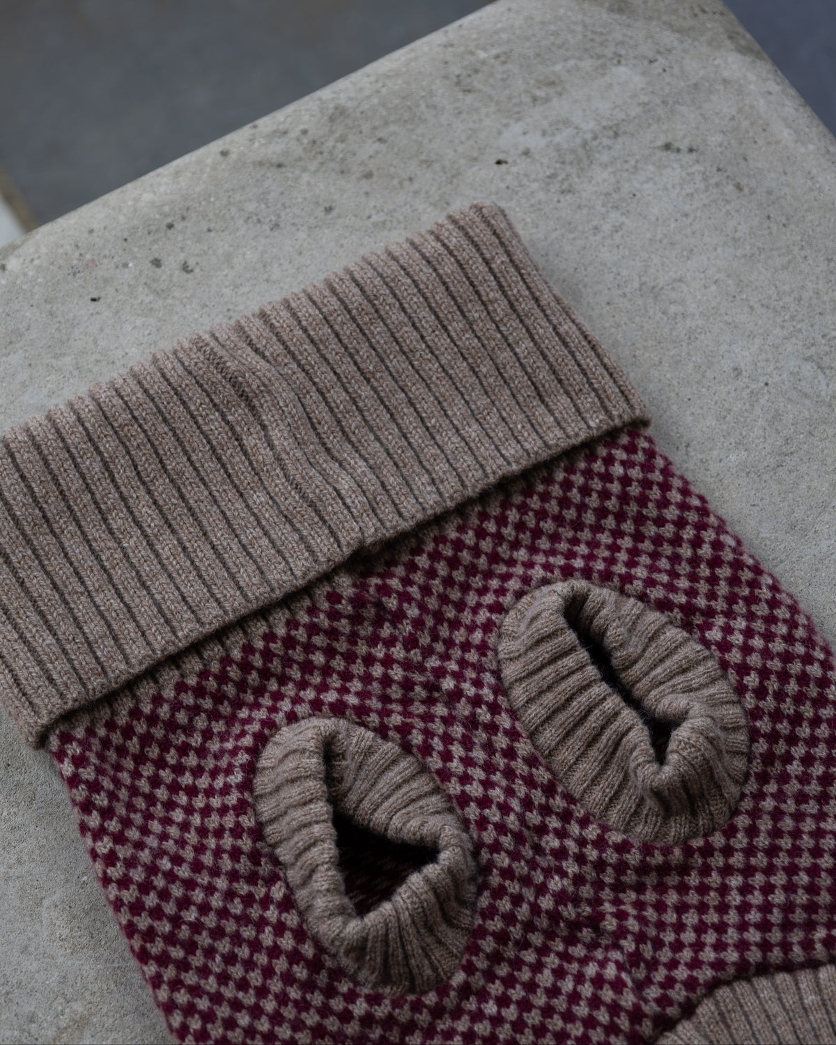 A close-up of a knit dog sweater in burgundy on a stone wall
