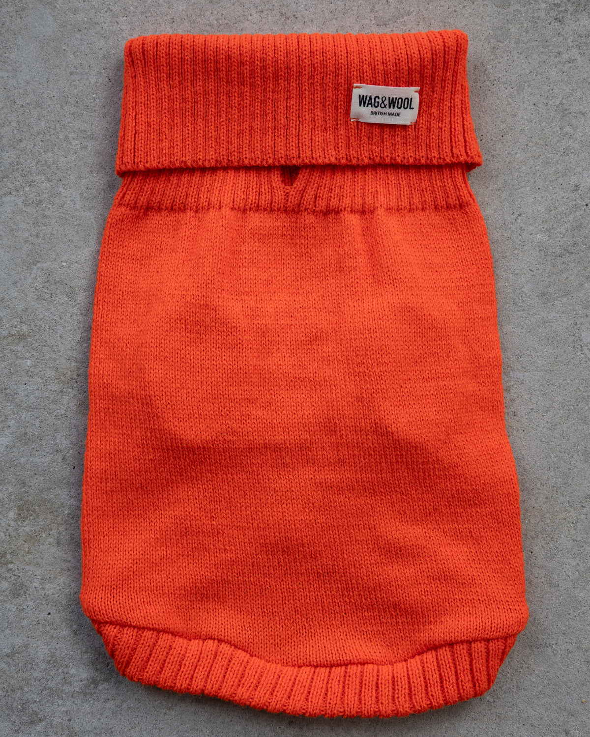 Bright orange knit pet sweater laid flat on a gray textured surface,
