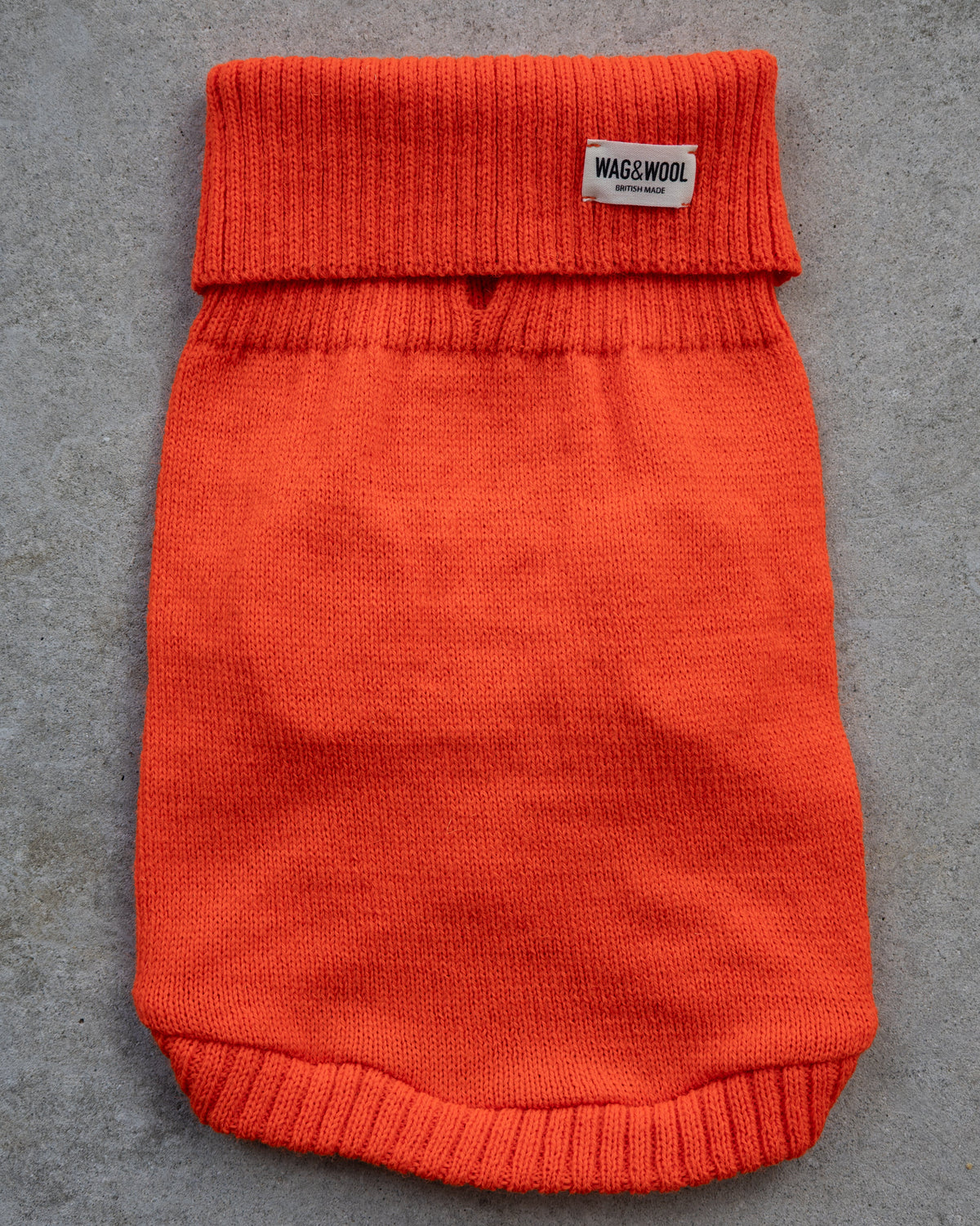 Bright orange knit pet sweater laid flat on a gray textured surface,