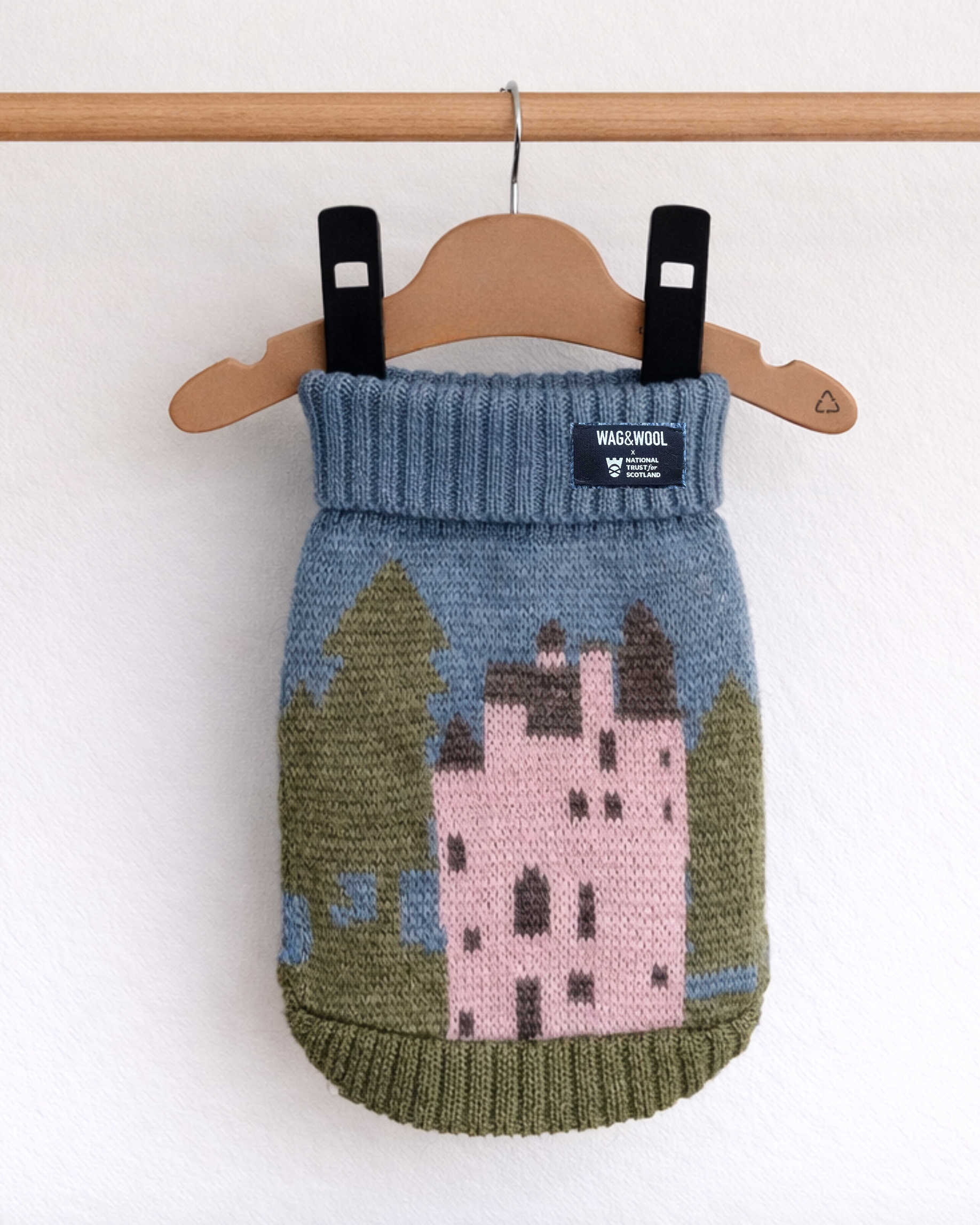 Knitted dog sweater with castle design on a hanger against a white background