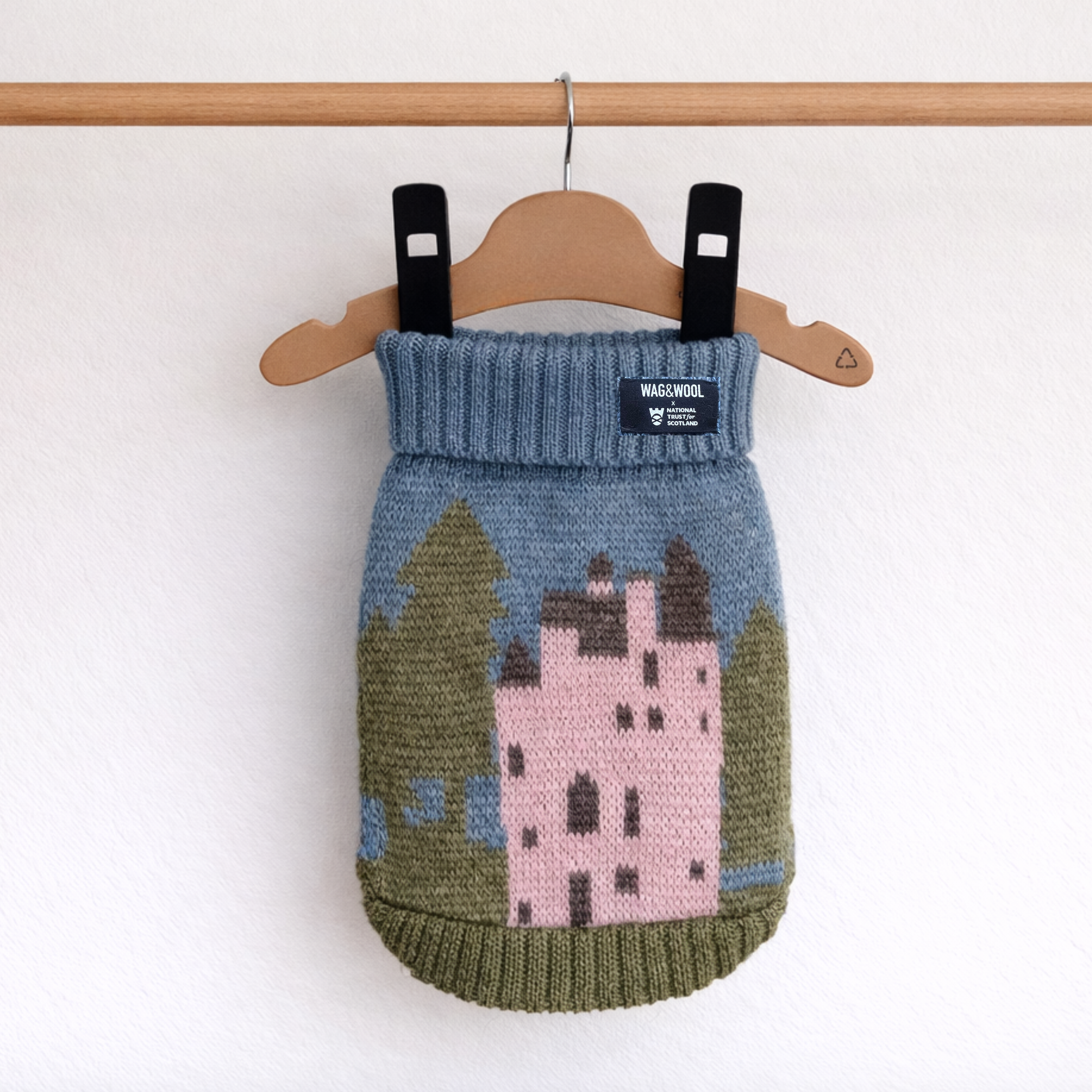 Knitted dog sweater with castle design on a hanger against a white background