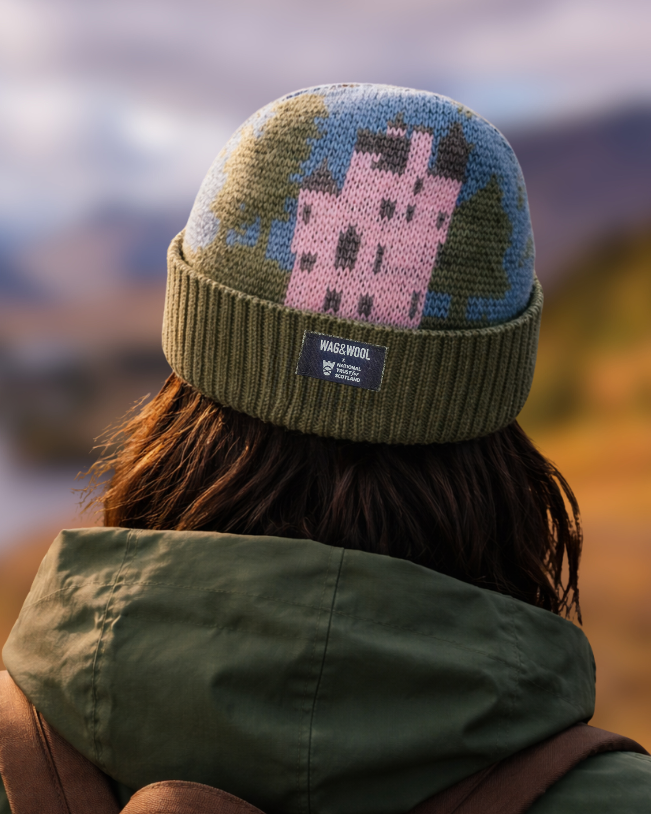 Person wearing a patterned beanie and green jacket with a blurred natural landscape in the background